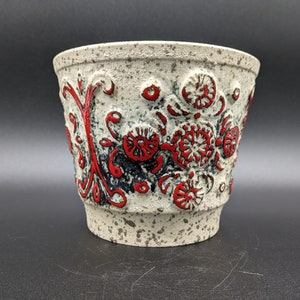 Peut inclure: Un pot en céramique blanche avec un glaçage moucheté et un motif floral rouge et noir.