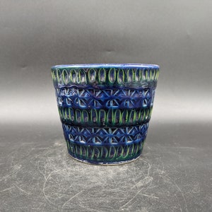 Può includere: Un vaso in ceramica blu e verde con un motivo geometrico. Il vaso ha una base larga e un'apertura stretta.