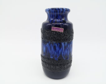 May include: A blue and black ceramic vase with a textured finish. The vase has a label that reads "scheurich".
