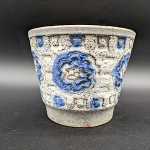 Könnte beinhalten: Ein weißer Keramiktopf mit blauem Blumendesign. Der Topf hat eine strukturierte Oberfläche und einen leicht ausgestellten Rand.