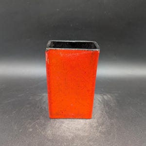 Peut inclure: Un récipient rectangulaire rouge avec un intérieur noir. Le récipient a une surface texturée et un aspect légèrement usé. L'objet est placé sur un fond sombre.