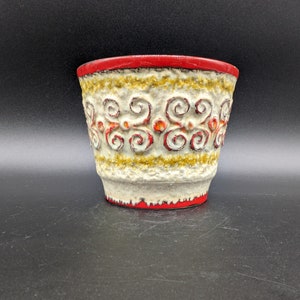 May include: A white ceramic planter with a red rim and a decorative pattern of red and gold swirls. The planter is on a black background.