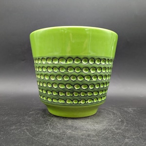 May include: A green ceramic planter with a textured band of raised circles. The planter has a glossy finish and a rounded shape. The color is a bright, vibrant green, with a darker green pattern around the middle.