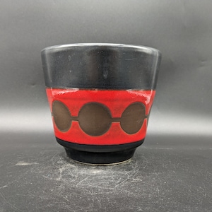 Könnte beinhalten: Ein schwarzer und roter Keramiktopf mit geometrischem Muster. Der Topf hat eine breite Öffnung und einen schmalen Boden.