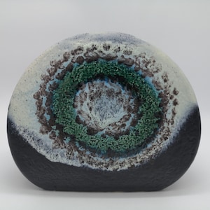 Puede incluir: Un jarrón de cerámica con un diseño abstracto único. El jarrón tiene forma de semicírculo y presenta un patrón de remolino en negro, blanco, azul y verde.