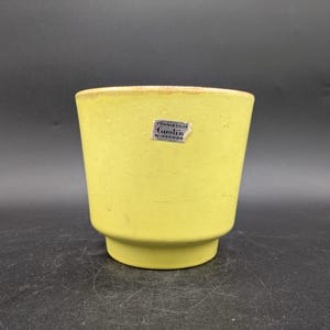 Peut inclure: Un pot en céramique jaune avec une étiquette indiquant "Gumnieshop Caefern, Allemagne de l'Ouest".