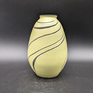 Könnte beinhalten: Eine gelbe Keramikvase mit schwarzen, wellenförmigen Linien. Die Vase ist oval geformt und hat eine glatte, matte Oberfläche.