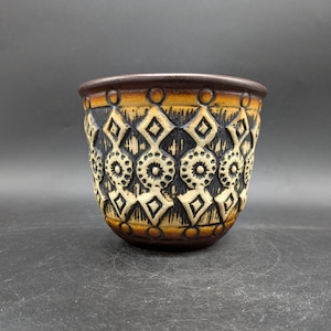 May include: A brown ceramic planter with a geometric pattern in black and white. The planter has a rounded bottom and a wide rim.