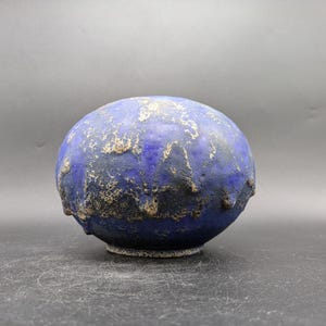 Könnte beinhalten: Eine kleine, runde Keramikvase mit einer blauen und schwarzen Glasur. Die Vase hat eine strukturierte Oberfläche und einen leicht unebenen Rand.