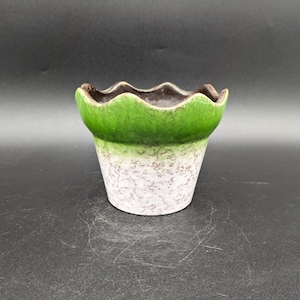 Puede incluir: Un pequeño macetero de cerámica verde y blanco con un borde festoneado. El macetero tiene un esmalte moteado y un borde marrón.