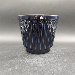 Könnte beinhalten: Ein dunkelblauer Keramiktopf mit einem strukturierten Design aus vertikalen Linien und kleinen, abgerundeten Formen. Der Topf hat einen leicht ausgestellten Rand und einen glatten, abgerundeten Boden.