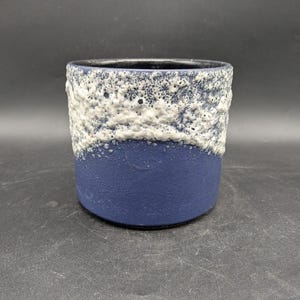 May include: A ceramic planter with a textured white and blue design. The top half of the planter has a textured white pattern, while the bottom half is a solid blue. The interior is black.