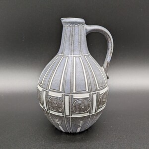 May include: A blue and white ceramic pitcher with a geometric design. The pitcher has a rounded body and a handle.