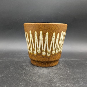 May include: A brown ceramic planter with a white geometric pattern. The planter has a rounded bottom and a wide opening.