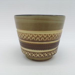Puede incluir: Una maceta de cerámica marrón con un patrón geométrico en tonos marrones, beige y naranja.