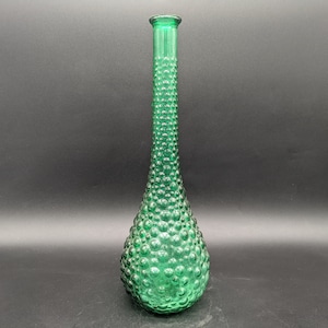 Puede incluir: Una botella de vidrio verde alta con una superficie texturizada con forma de burbujas. La botella tiene un cuello estrecho y una base redondeada.