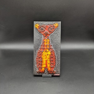May include: A ceramic wall tile featuring a raised design of a stylised animal in orange, yellow and black. The tile has a textured surface and the word "Ceramundo" is printed in red at the bottom.