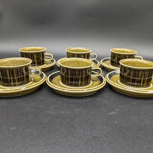 Peut inclure: Six tasses à thé en céramique rayées brun et noir avec des soucoupes assorties. Les tasses et les soucoupes ont un aspect rustique et terreux.