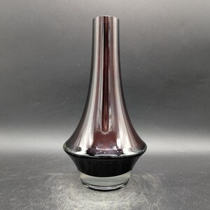May include: A tall, elegant vase with a flared base and a slender neck. The vase has a dark, metallic finish that transitions from a deep burgundy to a black base. The glass is clear at the bottom.