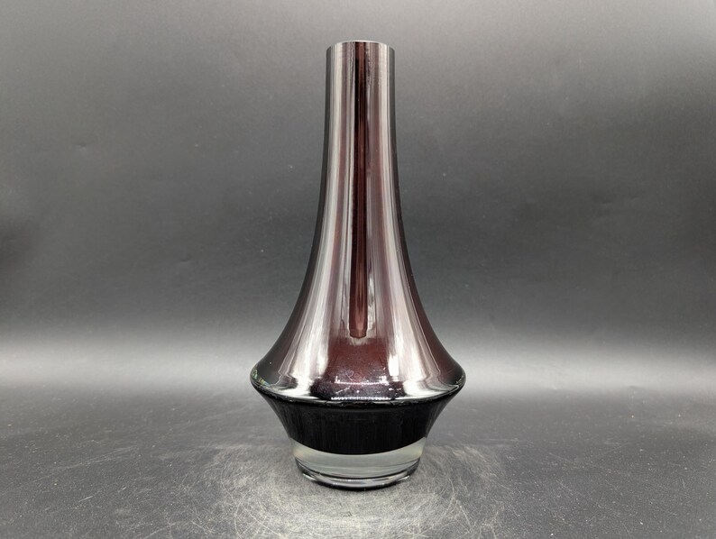 May include: A tall, elegant vase with a flared base and a slender neck. The vase has a dark, metallic finish that transitions from a deep burgundy to a black base. The glass is clear at the bottom.
