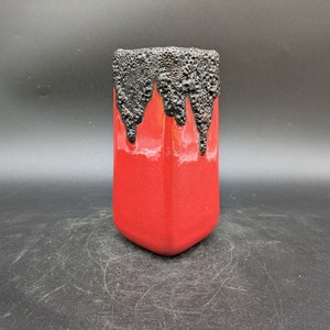 Puede incluir: Un jarrón de cerámica rojo con un esmalte negro que gotea por los lados. El esmalte tiene una apariencia texturizada y burbujeante.