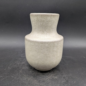 Peut inclure: Un petit vase en céramique gris avec une surface texturée. Le vase a un corps arrondi et un col étroit.