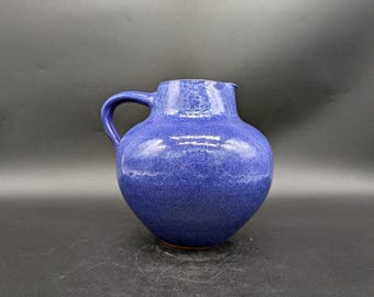 May include: A blue ceramic pitcher with a speckled glaze and a rounded body. The pitcher has a handle and a wide opening.