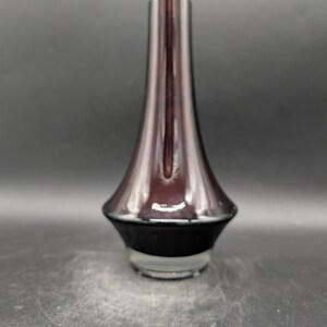 May include: A tall, elegant vase with a flared base and a slender neck. The vase has a gradient color scheme, transitioning from a dark, opaque base to a translucent, reddish-brown upper portion. The vase is made of glass and has a glossy finish.