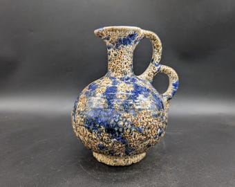 May include: A ceramic vase with a round body, a spout, and two handles. The vase has a speckled pattern in shades of blue, brown, and beige. The vase is a decorative item.