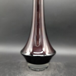 May include: A tall, elegant vase with a flared base and a slender neck. The vase features a gradient of colors, transitioning from a deep burgundy at the top to a black base, with a clear glass bottom. The design is modern and minimalist.