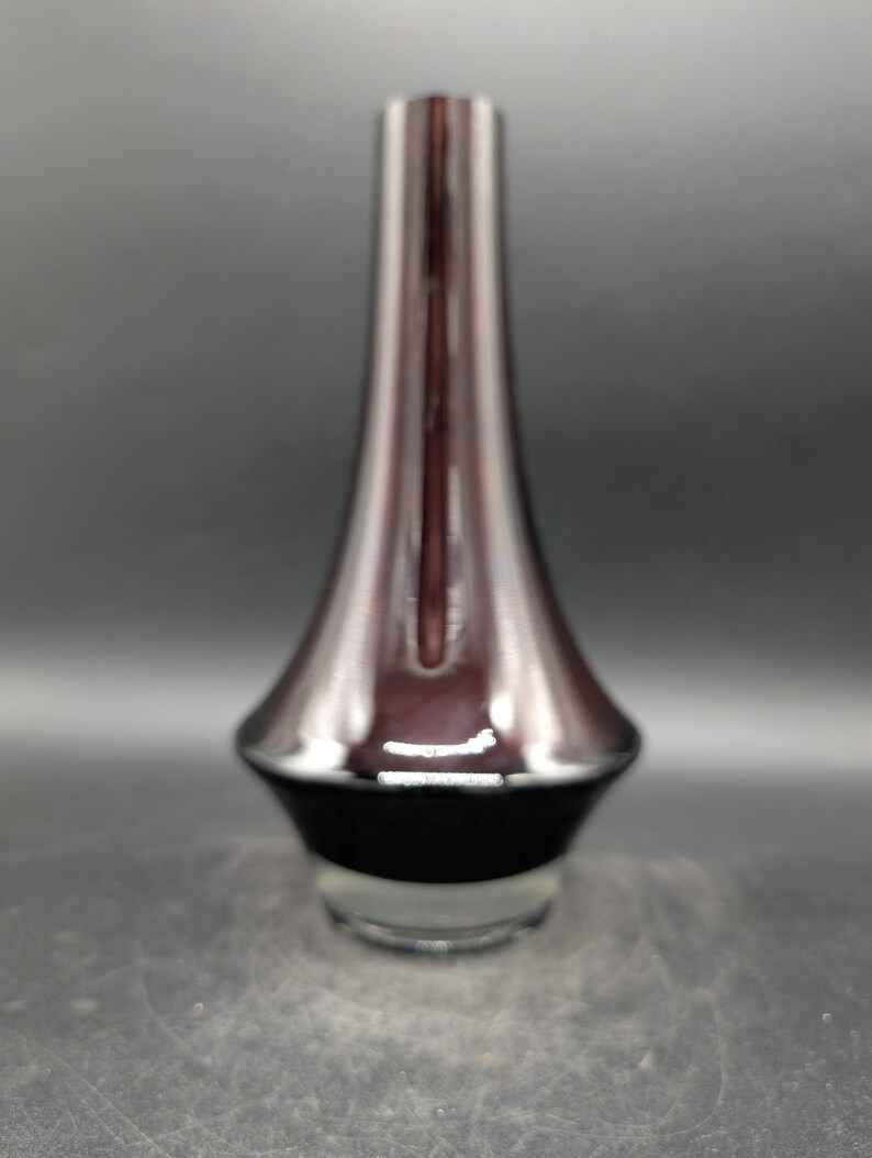 May include: A tall, elegant vase with a flared base and a slender neck. The vase features a gradient of colors, transitioning from a deep burgundy at the top to a black base, with a clear glass bottom. The design is modern and minimalist.