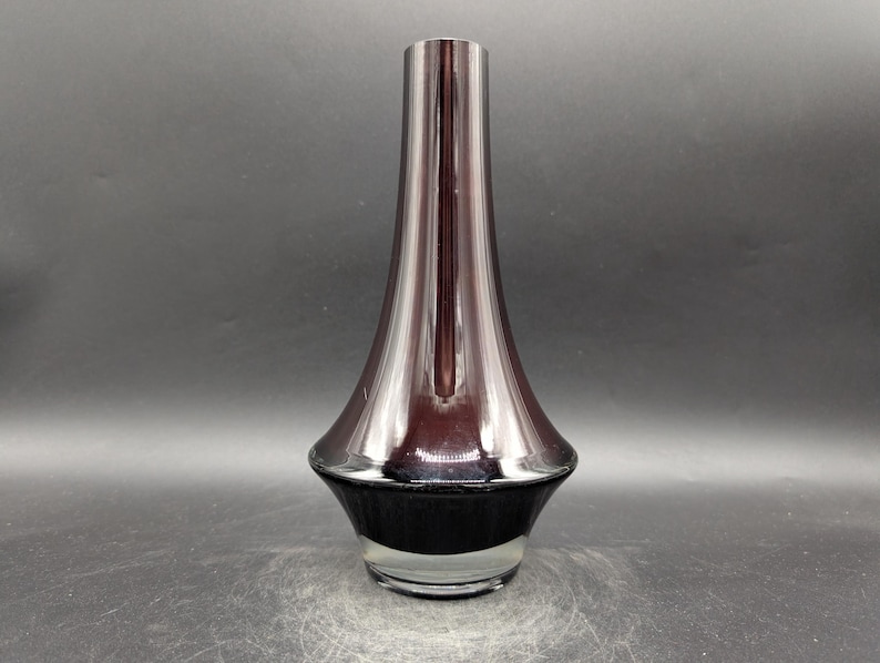 May include: A tall, elegant vase with a flared, metallic burgundy body and a black base. The vase has a sleek, modern design, perfect for displaying flowers or as a decorative accent. The vase is made of glass and has a clear, transparent base.