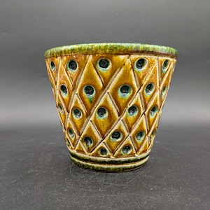 Puede incluir: Una maceta de cerámica con un patrón de diamante y esmalte verde y marrón. La maceta tiene pequeños agujeros en todo el diseño.