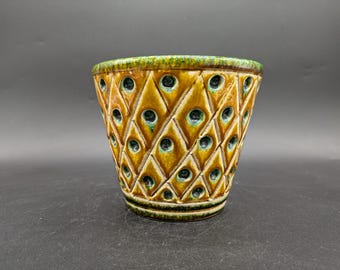 May include: A ceramic planter with a diamond pattern and green and brown glaze. The planter has small holes throughout the design.
