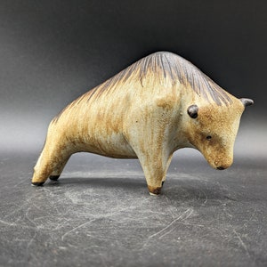 May include: A ceramic sculpture of a brown and black bull with a textured surface. The bull is standing on a gray surface.