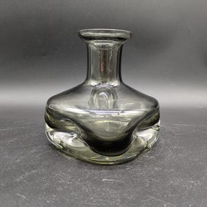 Può includere: Un vaso di vetro trasparente con un design testurizzato e ondulato. Il vaso ha una base larga e un collo stretto.