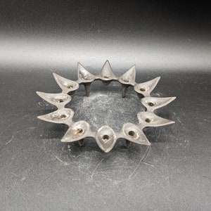 May include: A black metal candle holder with 12 points, resembling a sun or star. Each point has a small cup for holding a candle.