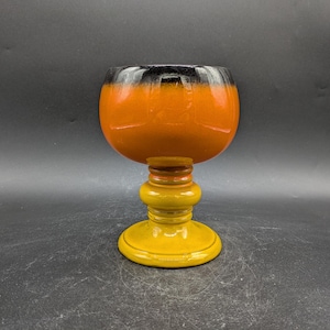 Könnte beinhalten: Ein Keramikkelch mit schwarzer und orangefarbener Glasur. Der Kelch hat eine breite Schale und einen hohen, schlanken Stiel. Die Basis des Kelchs ist eine solide, runde Form.