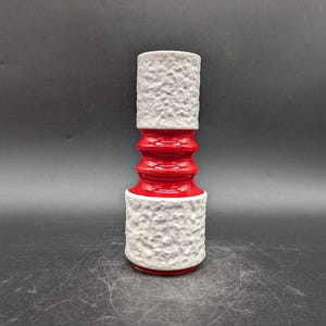 May include: A white ceramic vase with a textured surface and a red band around the middle. The vase has a cylindrical shape and is approximately 25 cm tall.