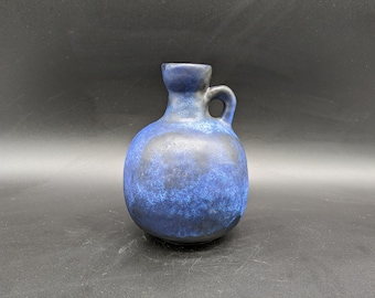 May include: A blue ceramic vase with a speckled glaze and a handle. The vase has a rounded body and a narrow neck.