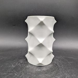 May include: White ceramic vase with a geometric diamond pattern. The vase is cylindrical and has a smooth, matte finish.