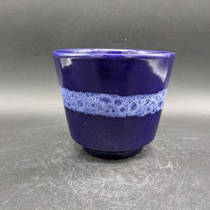 May include: A dark blue ceramic cup with a white band around the middle. The band has a textured, bubbly design.