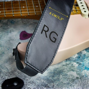 May include: Black leather guitar strap with the initials "RG" embossed in white. The strap is 6 cm/2.5 inches wide.