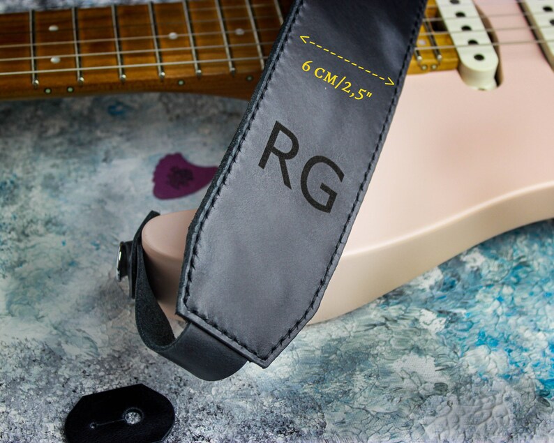 May include: Black leather guitar strap with the initials "RG" embossed in white. The strap is 6 cm/2.5 inches wide.