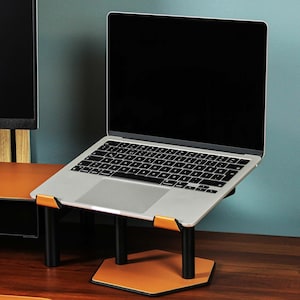 Peut inclure: Un ordinateur portable est surélevé sur un support en métal noir avec une base en cuir marron. Le support a une forme hexagonale et l'ordinateur portable est posé sur une surface en bois.