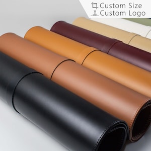 以下が含まれることがあります： 黒、茶色、ベージュ、ボルドーなど、さまざまな色の巻き上げられた革製マウスパッド6枚のクローズアップ。マウスパッドは一列に並べられており、黒色のものが手前にあります。背景には「Custom Size Custom Logo」というテキストが表示されています。