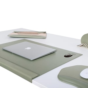 Op de afbeelding: Een groene leren bureau mat met een luiaard ontwerp en de tekst "procrastination station". Een laptop computer ligt op de mat.