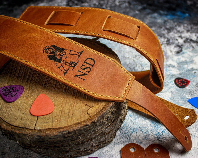 May include: A brown leather guitar strap with a  personalized inscription that reads "NSD" and a small illustration of a pirate.