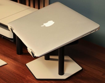 May include: A silver laptop computer rests on a black and white hexagonal stand. The stand has black cylindrical legs and a white base. The laptop is angled upwards, displaying the Apple logo. The stand is on a wooden surface.
