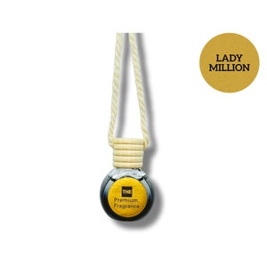 May include: A black glass car air freshener with a gold label that says "THE Premium Fragrance" hanging from a white rope. The air freshener is labelled "Lady Million".